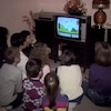 Un groupe d'enfants sont tournés vers un écran de téléviseur sur lequel se déroule une partie du jeu Mario Bros sur console Nintendo.