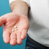 On voit la main d'un homme, ouverte, dans laquelle se trouvent trois comprimés.