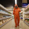 Un homme en combinaison de protection vaporise un produit désinfectant dans les allées d'une épicerie. 