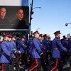 Un cortège de policiers marche au pas devant un immeuble où est affichée la photo de Brett Ryan et Travis Jordan.