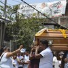 Une femme asperge un cercueil porté par des hommes dans une rue devant une banderole électorale d'Alfredo Cabrera, le défunt.