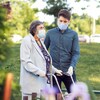 Un jeune homme masqué aidant une aînée à se déplacer dehors.