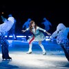 Une femme portant un costume de patineuse artistique est entourée de plusieurs patineurs lors d'un spectacle sur glace. 