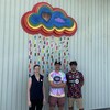 Trois personnes devant un mur décoré d'un nuage et de papiers collés aux couleurs de l'arc-en-ciel.