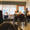 Des personnes âgées assisent dans des fauteuils roulants dans une salle.