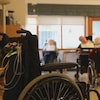 Quatre résidents en fauteuil roulant et une infirmière sont dans une salle.