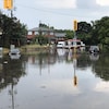 Des véhicules tentent de circuler sur une rue inondée. 