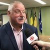 Le député néo-écossais Darrell Samson parle en entrevue. Derrière lui, on peut voir des drapeaux de la Nation métisse, fransaskois, saskatchewanais, et canadien. 