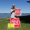 Denise Melanson tient des pancartes anti-fracturation hydraulique. On voit une rivière derrière elle. 
