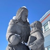 Une sculpture en granit devant un bâtiment, qui représente une femme et un enfant avec un livre à la main.
