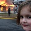 Une petite fille regarde l'objectif de la caméra avec un air coquin alors qu'un feu ravage une maison derrière elle. 