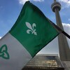Un drapeau franco-ontarien tenu devant la Tour CN à Toronto.
