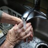 De l'eau coule du robinet sur des mains d'une personne âgée.