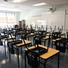 Des chaises à l'envers sur des rangées de pupitres dans une salle de classe.