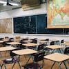 Une salle de classe vide avec un tableau, des tables et des chaises.