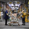 Des travailleurs de GM utilisent l'automatisation de l'assistance humaine pour souder des portes de véhicules à l'usine d'assemblage de General Motors.
