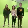 Trois adolescents debout sur le plancher peint en vert, devant les murs peints en vert, d'un studio de cinéma à leur école.