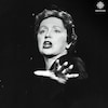 Édith Piaf chante avec une main devant elle. 
