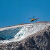 Un hélicoptère transportant des secouristes survole le glacier.