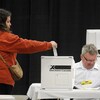 Une femme met son bulletin de vote dans une boîte de scrutin décorée du logo d'Élections Canada.