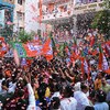 Une foule en liesse dans une rue sous une pluie de confettis, brandit des drapeaux du BJP.