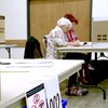 Deux personnes assises à un bureau sur lequel est déposée une urne électorale.