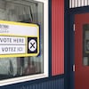 Une pancarte collée sur une fenêtre annonçant qu'il est possible de voter à cet emplacement.