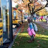 Une élève se dirige vers la porte ouverte d'un autobus scolaire stationné derrière deux autres autobus.