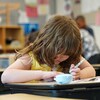 Une fillette est à son bureau dans une classe. Elle tient un crayon dans sa main gauche. Elle a la tête baissée vers des feuilles et semble très concentrée, le 18 mai 2022.