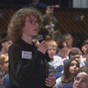 Un jeune avec un micro dans les mains, debout dans l'auditorium.