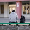 Un adolescent est assis sur un banc devant une école secondaire.