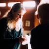 Une femme blonde penchée en avant sourit. 