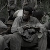 Un groupe d'hommes habillés en haillons mangent un repas en plein milieu d'un marais, dans une scène du film emancipation. 