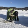 Deux pêcheurs installent une maisonnette sur la glace.