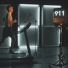 Émile Beauchemin court sur un tapis roulant. À droite de l'image, il y a une femme avec un micro. Le chiffre 911 apparaît sur une télévision. 