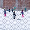Des enfants de niveau primaire qui jouent sur une butte de neige dans un cour d'école.