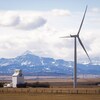 Paysage du sud de l'Alberta avec une éolienne en premier plan à côté d'un élévateur à grain et les montagnes Rocheuses en arrière-plan.