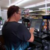 Une femme est debout derrière le comptoir d'une caisse dans une épicerie. 