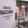 Une inscription du thème de l'exposition « Sous le racisme, un défi pour nos pensées au niveau supérieur d'un bâtiment ». 
