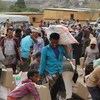 Des personnes dans un camp de réfugiés, avec des boîtes et des sacs de riz. 