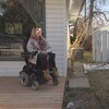Une femme en fauteuil roulant est devant sa maison et parle à une journaliste.