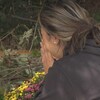 Une femme se tient assise avec les mains sur le visage devant des fleurs déposées sur le site de l'accident de voiture qui a emporté les trois hockeyeurs à Surrey.