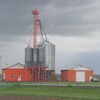 Une ferme de l'est ontarien avec des silos à grain et des bâtiments orange et blanc devant un ciel nuageux.