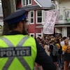 Une police regarde une foule de jeunes près d'une maison dans un quartier résidentiel, où une pancarte affiche « relaxez, nous sommes doublement vaccinés ».