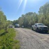 Deux camionnettes stationnées près d'une barrière sur un chemin de gravier, dans un secteur boisé.