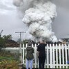 Des gens regardent un tas de ferraille brûler alors qu'une immense colonne de fumée s'en échappe.