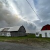 Une grange et un garage devant de l'épaisse fumée qui monte dans le ciel.