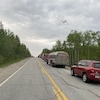 Un avion-citerne passe au-dessus d'une route sur laquelle sont stationnés des camions de pompiers et plusieurs autres véhicules.
