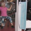 Un masque accroché à un poids, dans un centre de conditionnement physique. En arrière-plan, sur une machine de musculation, on voit une femme en train de s'entraîner.