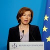 La ministre française des Armées, Florence Parly, en train de faire une déclaration derrière un lutrin sur lequel est écrit « République française ». Un drapeau de la France et de l'Union européenne sont accrochés derrière elle.